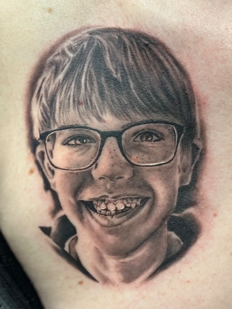 Porträt eines lächelnden Jungen mit Brille, der freudig in die Kamera schaut.marburg tattoo, tattoo marburg, tattoo studio marburg