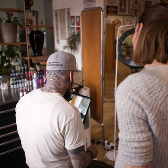 Eine tätowierte Hand zeichnet mit einem Pinsel auf Papier.marburg tattoo, tattoo marburg, tattoo studio marburg